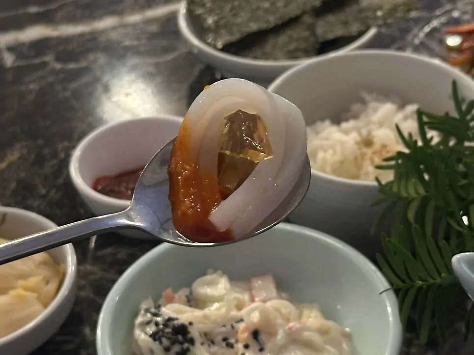 A piece of live squid sashimi topped with bonito flake jelly