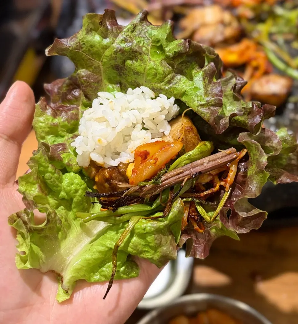 Ssam wrap stacked with pork belly, minari, bracken fern, and kimchi
