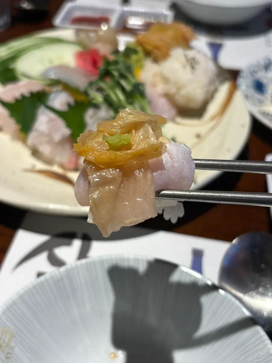 Chopsticks picking up a piece of halibut sashimi