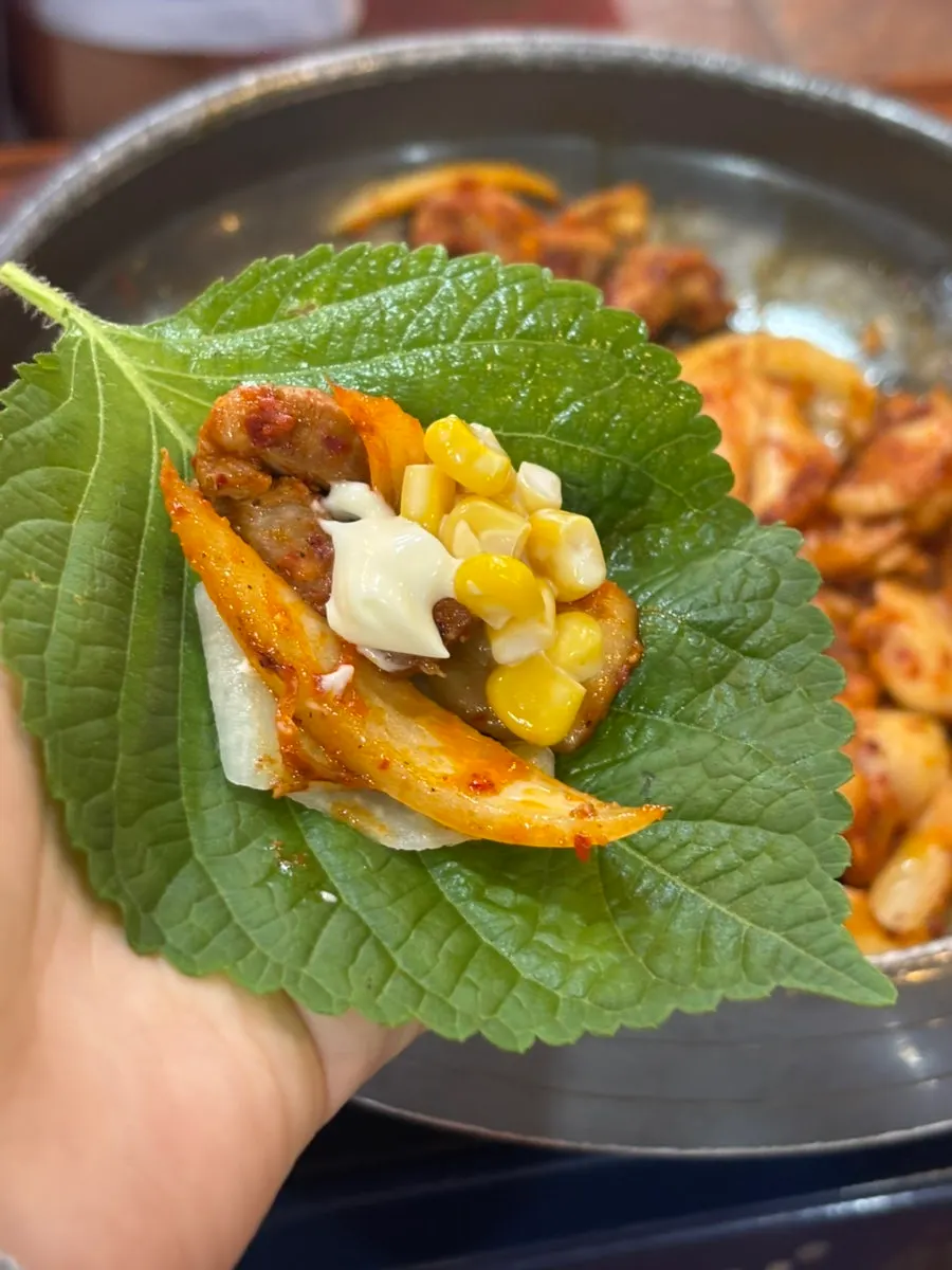 A bite of pork kimchi grill topped with corn kernels