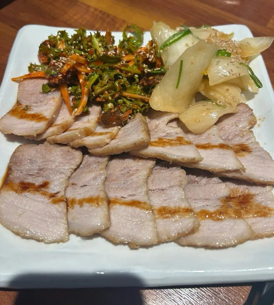 Plate of herbal boiled pork samhap with cockle salad and aged kimchi