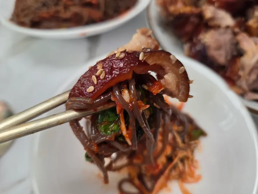 A chopstick-full of mak-guksu noodles coated in fruit sauce
