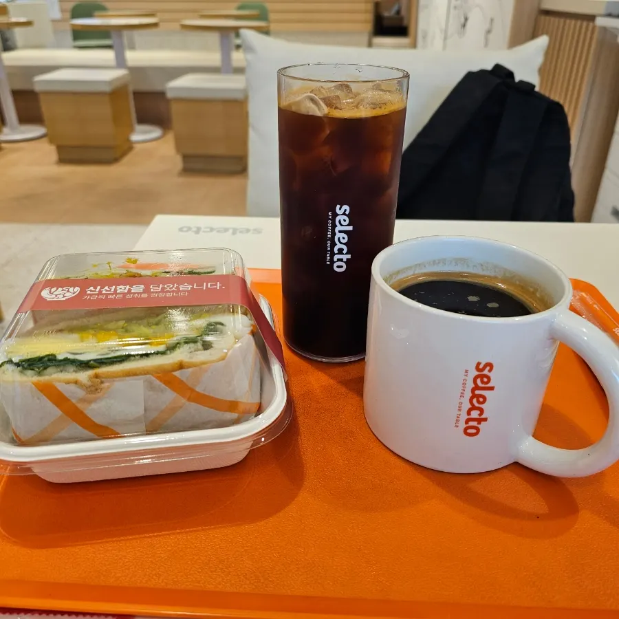 Two cups of americano and a sandwich on an orange tray