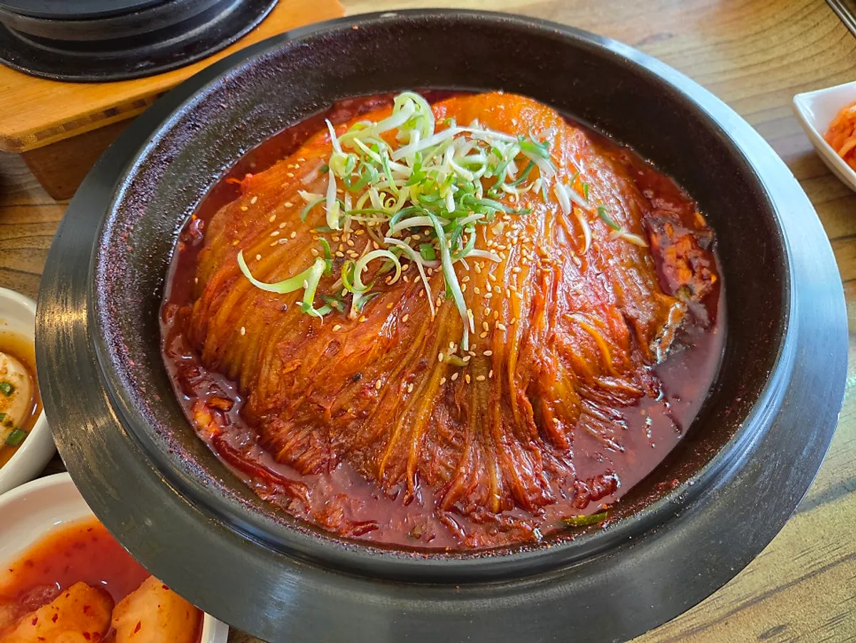 Pot of aged-kimchi braised mackerel topped with broad kimchi leaves