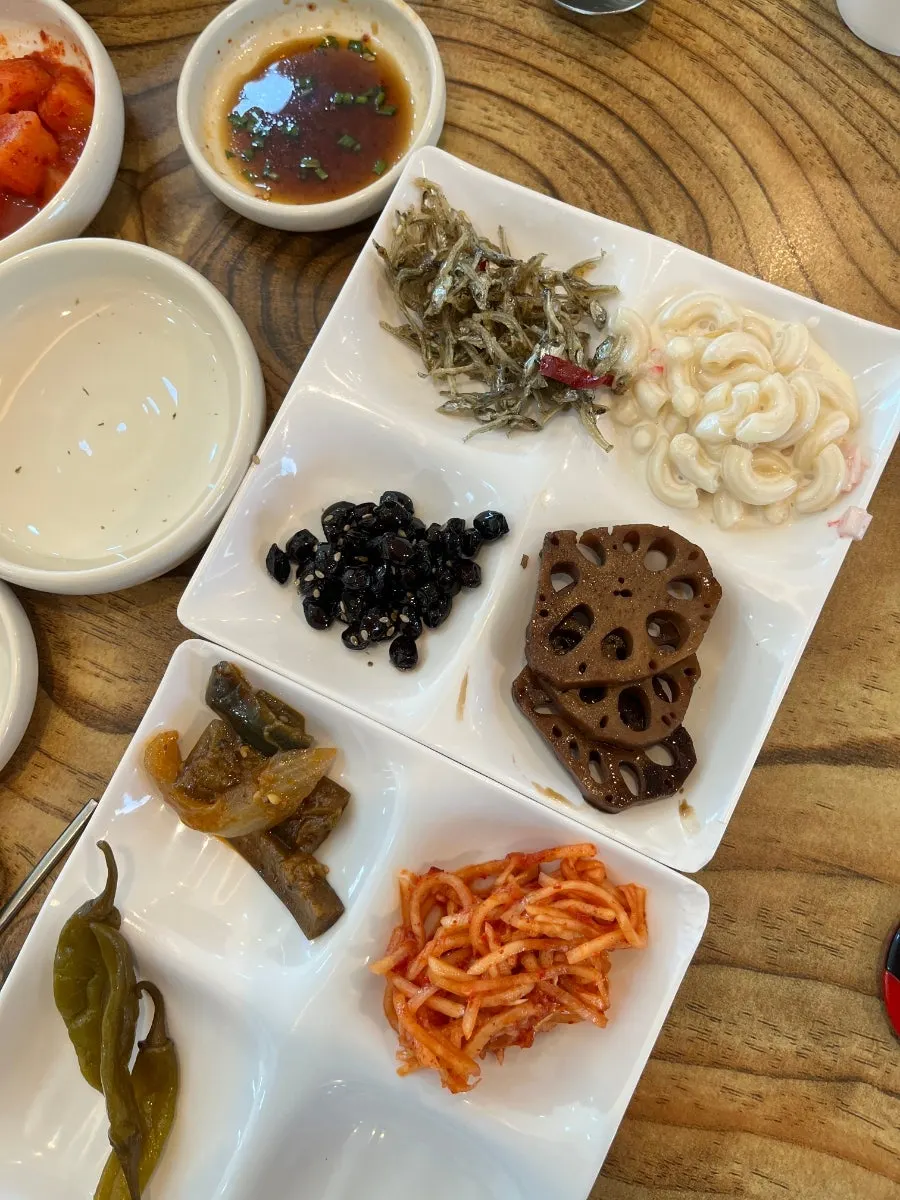 Self-serve side dishes including seasoned vegetables, salted seafood, and kimchi
