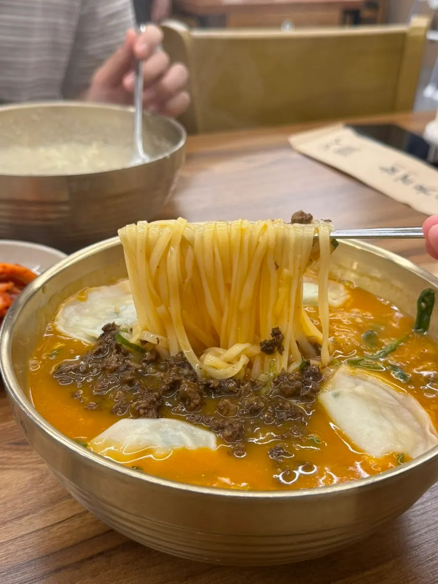 Eolkeun kalguksu topped with meat garnish and wonton dumplings