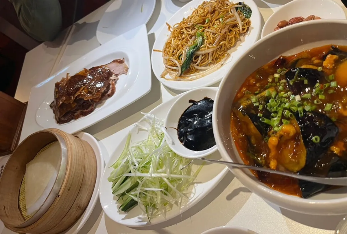 Table spread of half Peking duck, fish-fragrant eggplant, and egg noodles