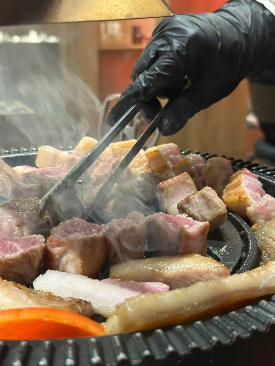 Thick cuts of meat grilling under the overhead hood