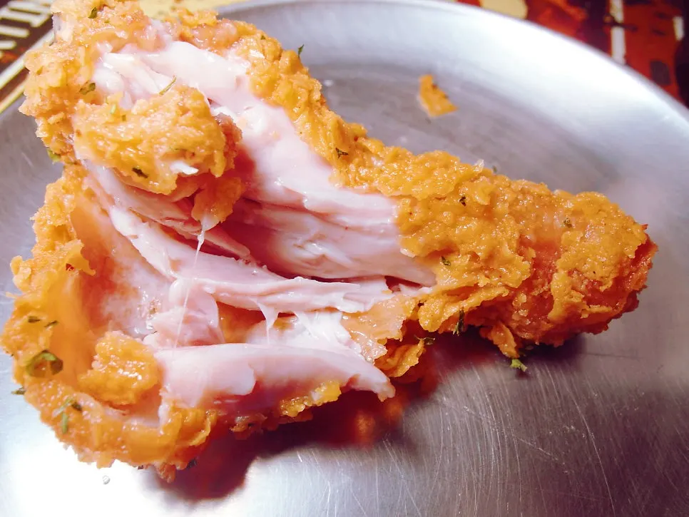 Chicken leg with batter pulled back to show the meat inside