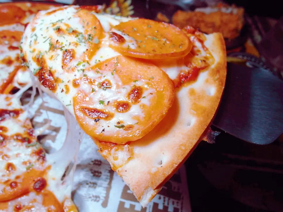 Slice of thin-crust pizza topped with pepperoni