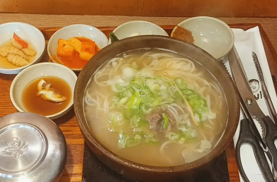 A full spread with rice and side dishes alongside the galbitang