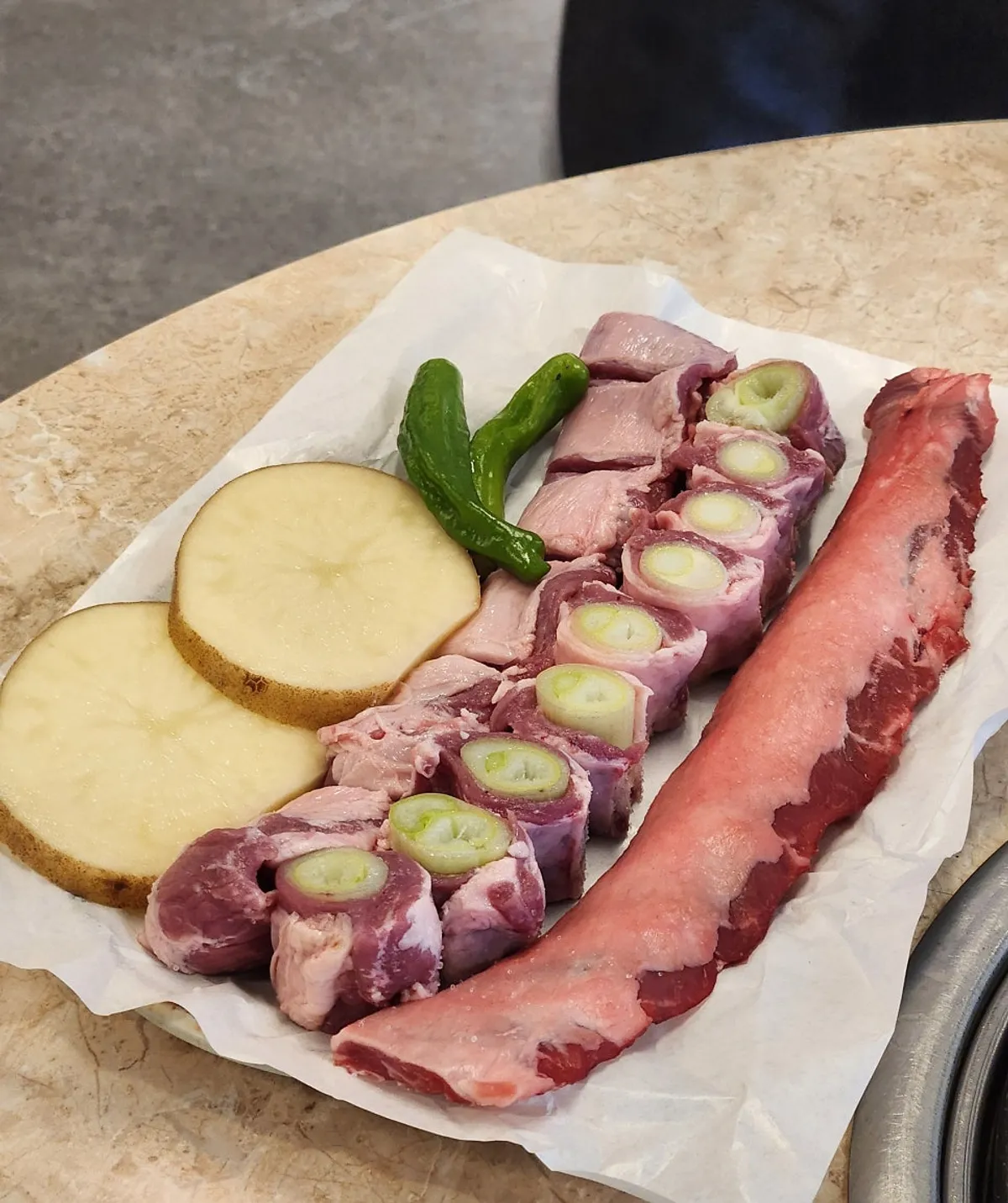 Plate of raw gamjagisal, green onion, and dry-aged cuts