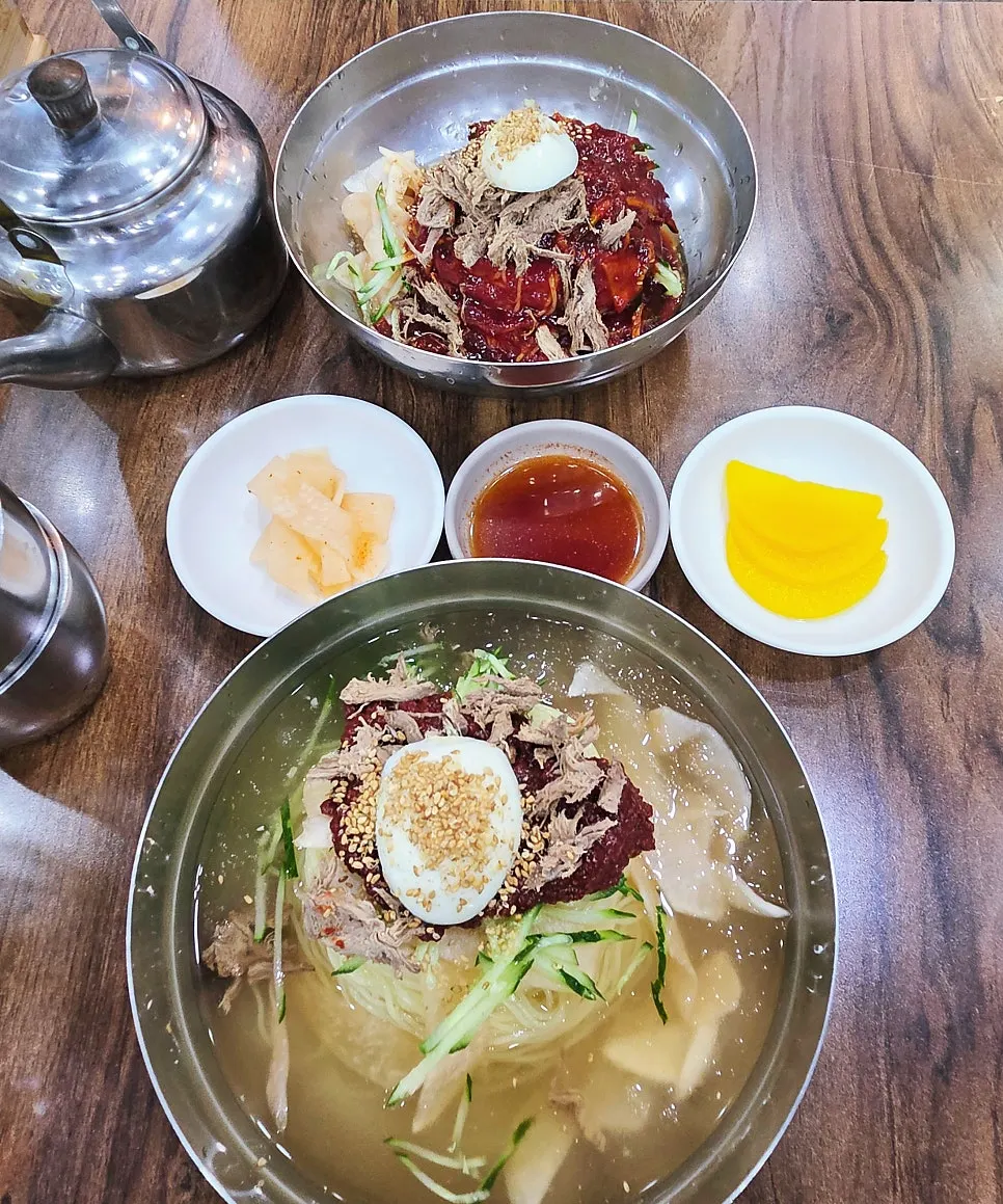 Two bowls of milmyeon and dumplings laid out on the table