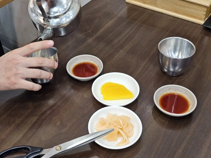 Basic table setting with warm broth, pickled radish, radish kimchi, and soy sauce dip