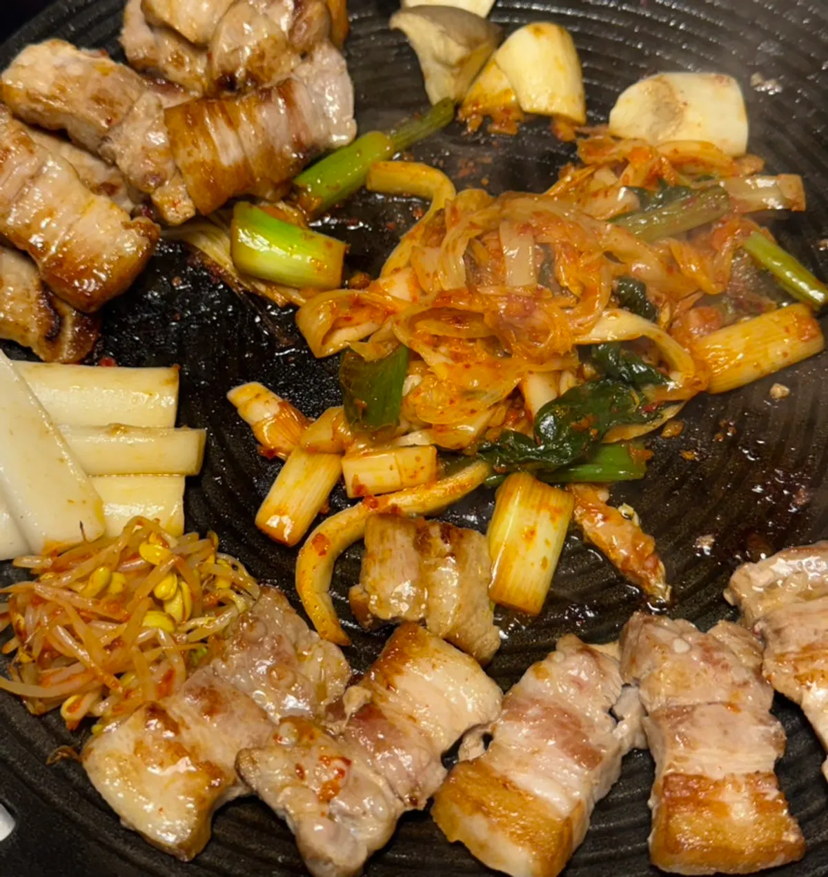 Pork belly, kimchi, and scallions cooking on the grill