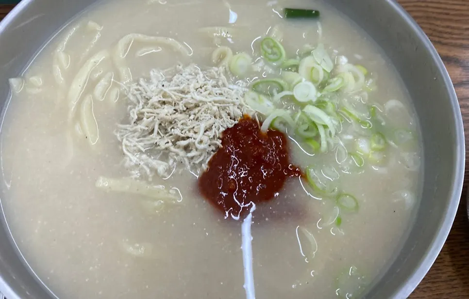 A bowl of spicy chicken kalguksu with pa gomyeong topping