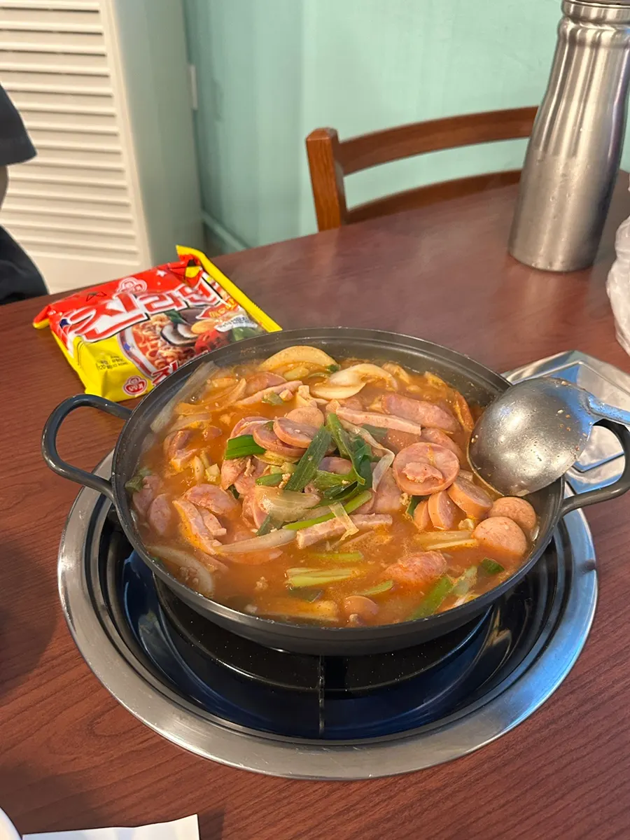 Clear budae jjigae broth loaded with green onions and vegetables