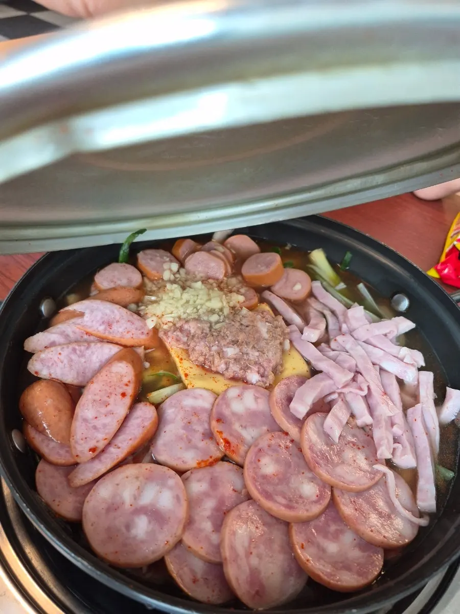 Budae jjigae before boiling, topped with green onion and vegetables