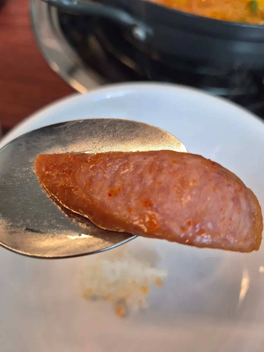 A spoonful of rice topped with ham and sausage