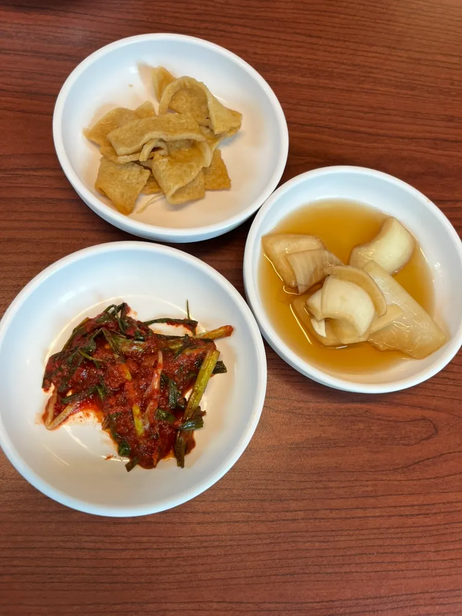 Self-serve side dish bar with pickled onion, fish cake, and green onion kimchi