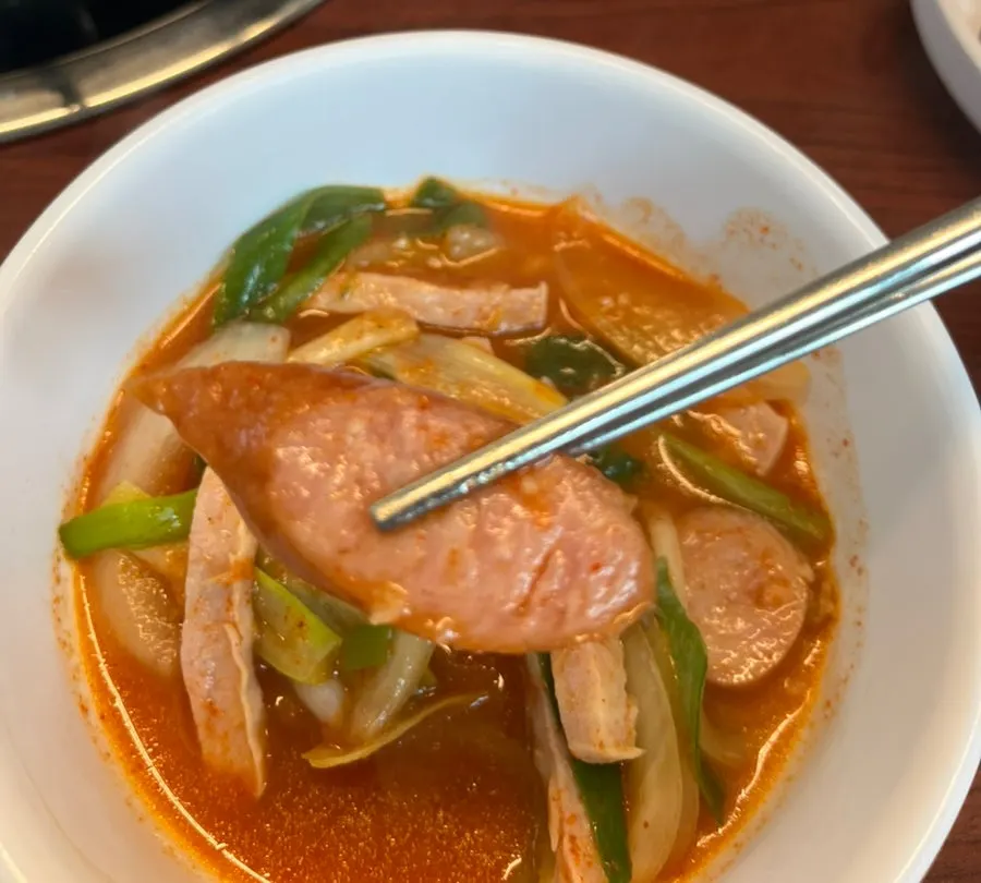A ladle scooping up budae jjigae broth