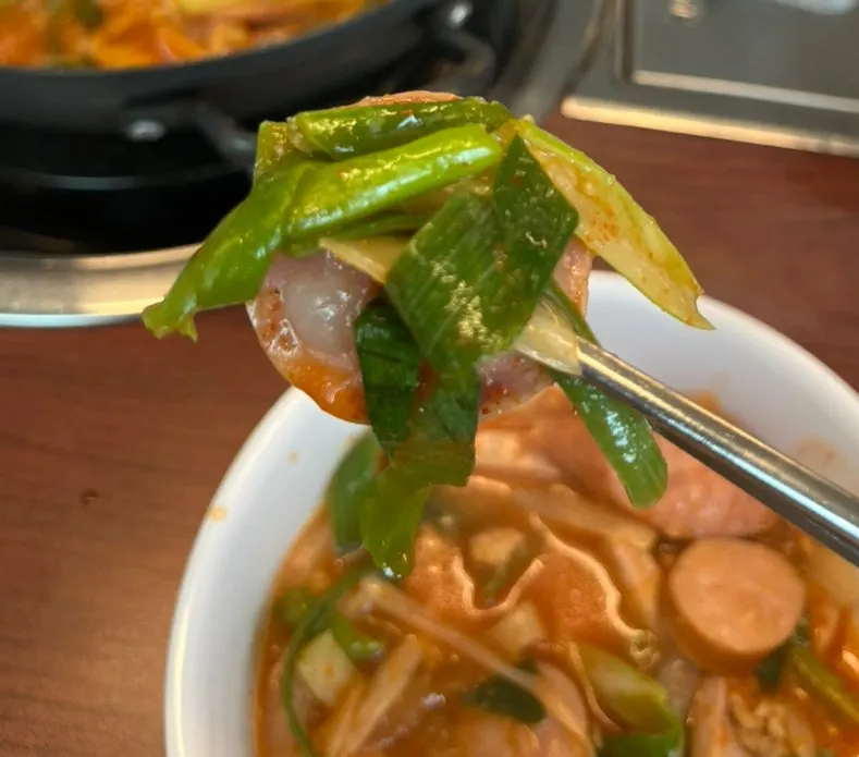 A spoon topped with vegetables and sausage