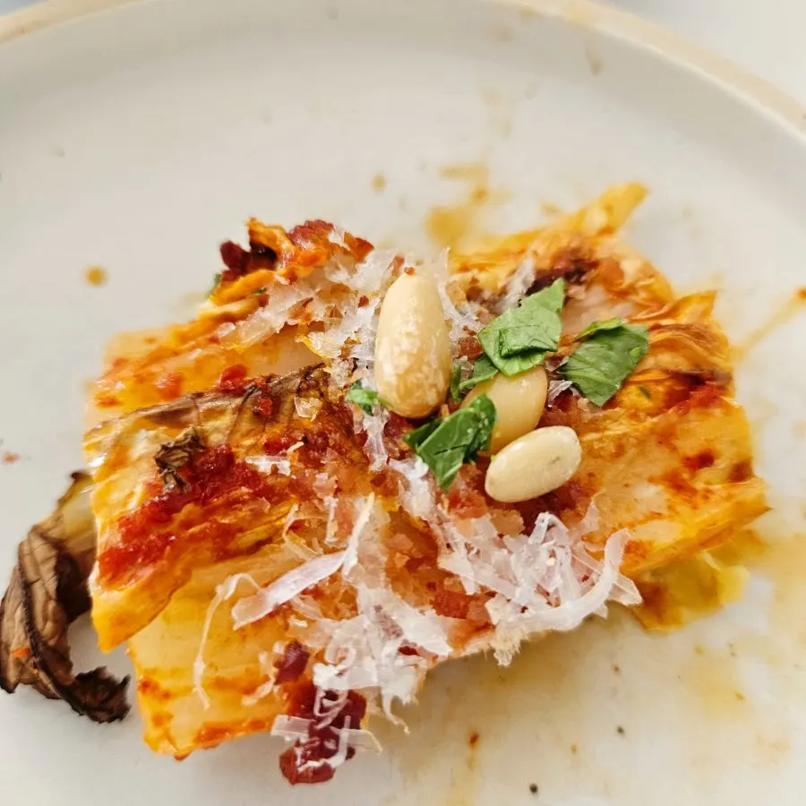 Grilled napa cabbage topped with cheese, perilla leaf, and pine nuts