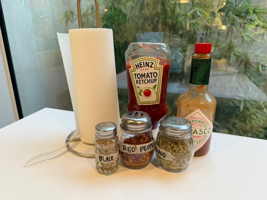 Black pepper, red pepper, ketchup, and hot sauce on the table
