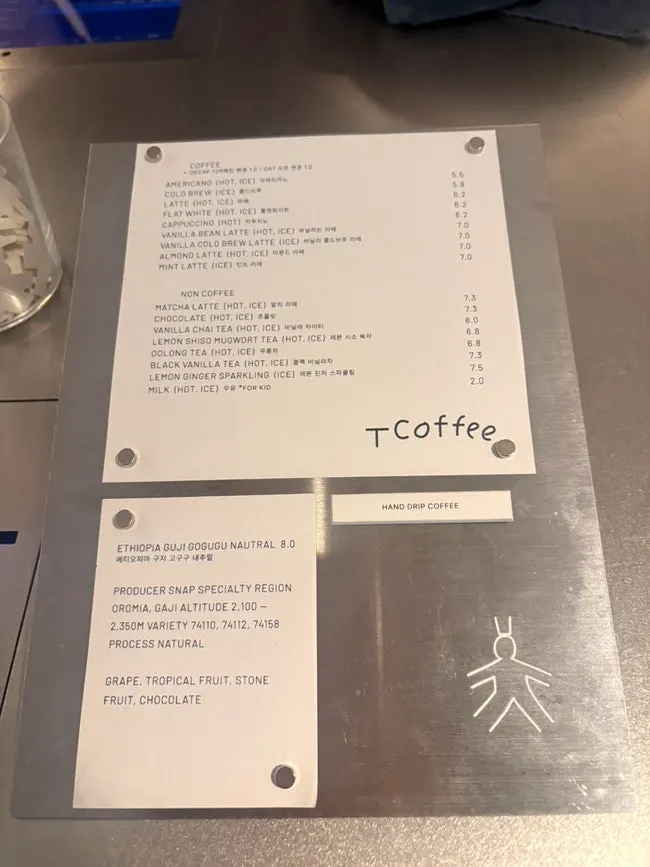 T Coffee's coffee menu board listing americano, cold brew, and latte