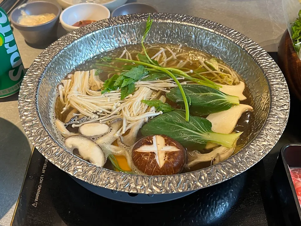 Vegetables cooking in clear mushroom broth in the shabu pot