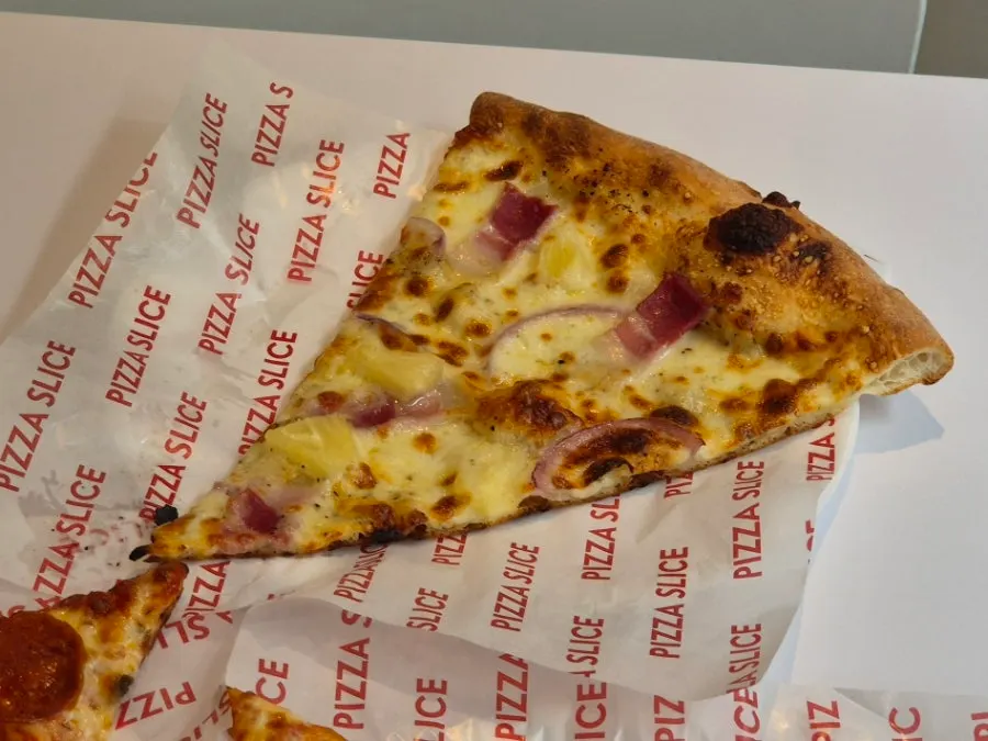 A slice of cheese pizza drizzled with hot sauce