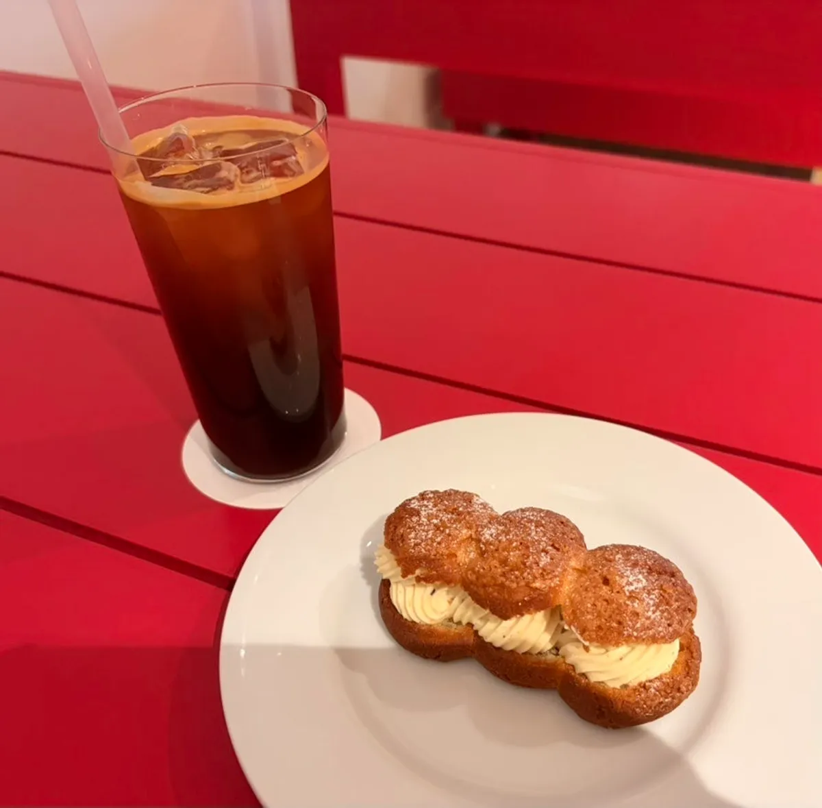 Iced americano and pistachio cream choux on the red table by the window