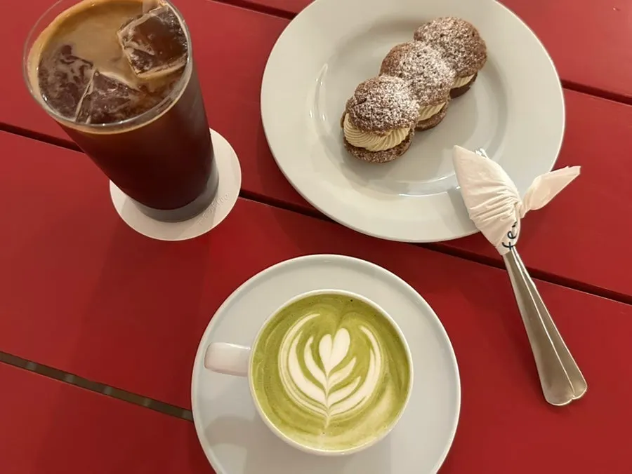 An americano, matcha latte, and cream puff on a red table