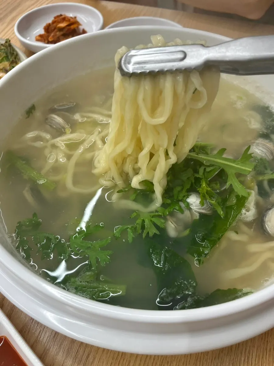 Clam kalguksu broth topped with clams and crown daisy greens