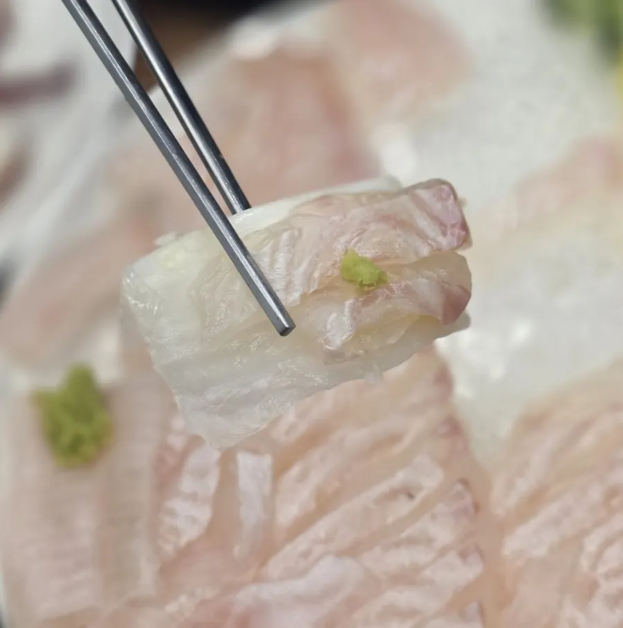 A piece of flounder sashimi dipped in chojang sauce