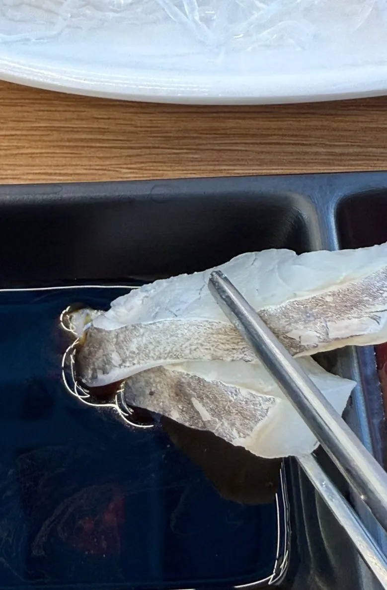 A slice of rockfish sashimi dipped in soy sauce