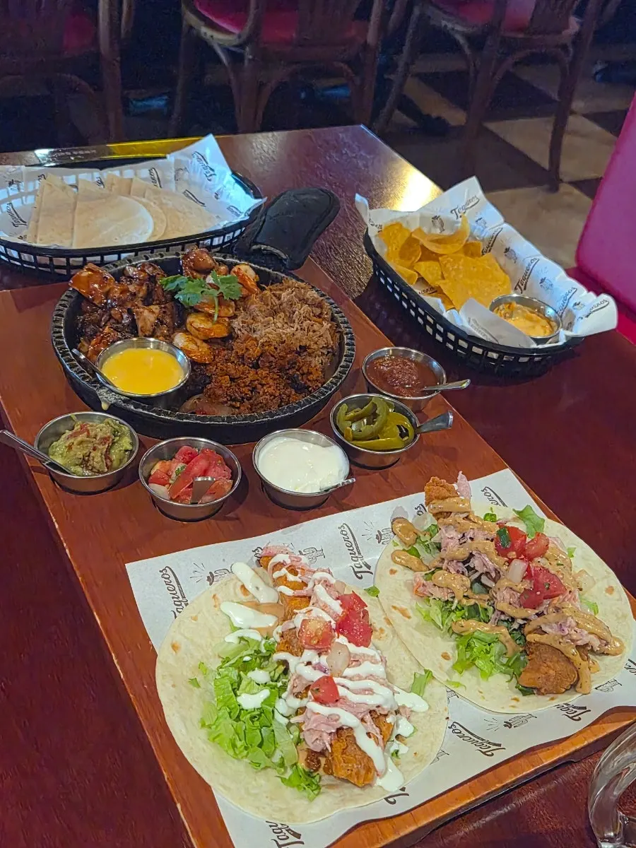 A spread of tortillas, fajita, sauces, chicken taco, and fish taco