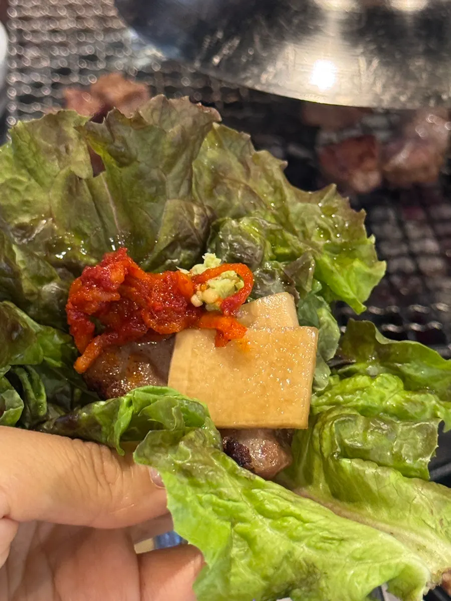 A lettuce wrap of meat with scallion salad, garlic, and ssamjang