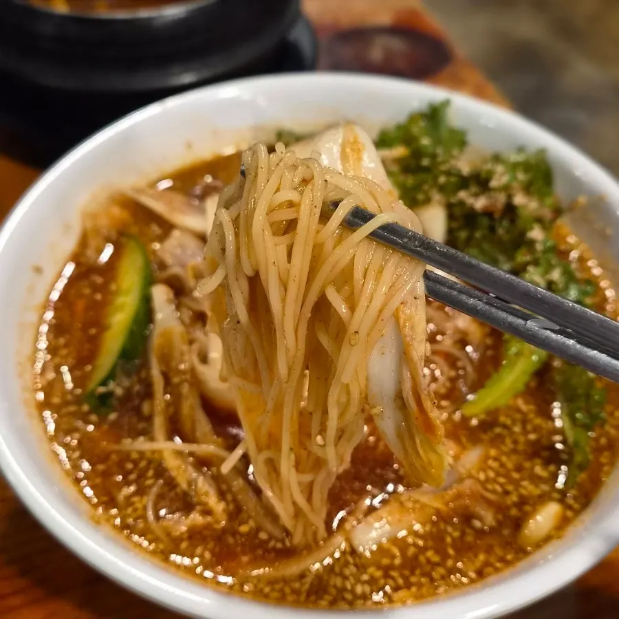 Spicy mixed noodles topped with white kimchi and cucumber