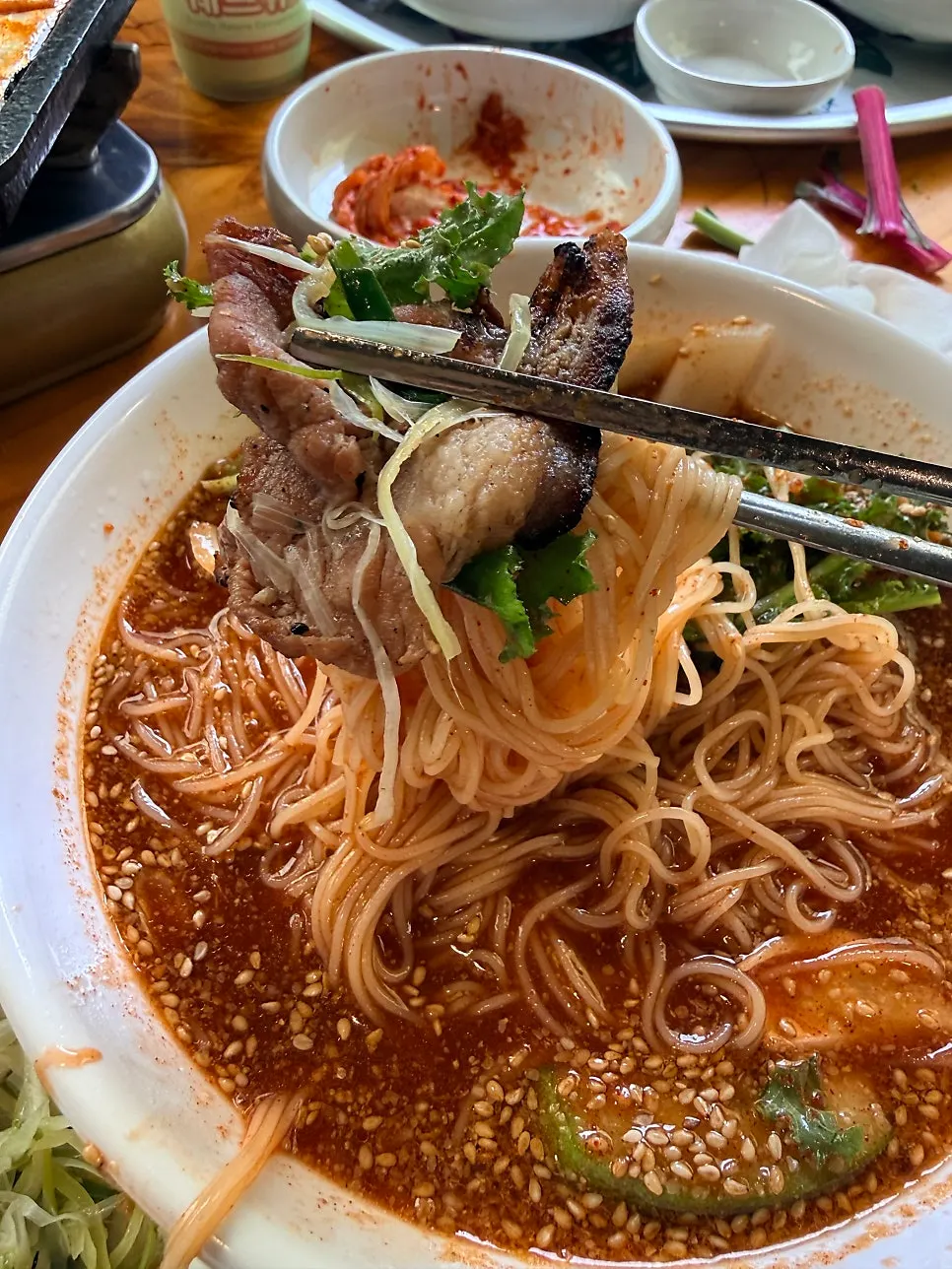 A chopstick-full of bibim noodles covered in sesame seeds