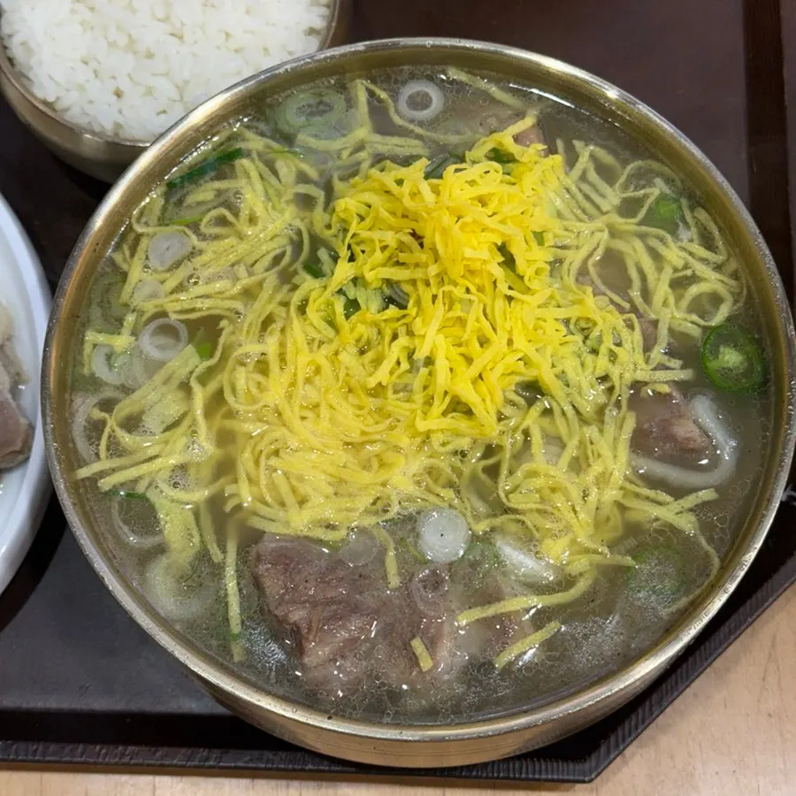 Bowl of bone kalguksu topped with egg garnish and scallions