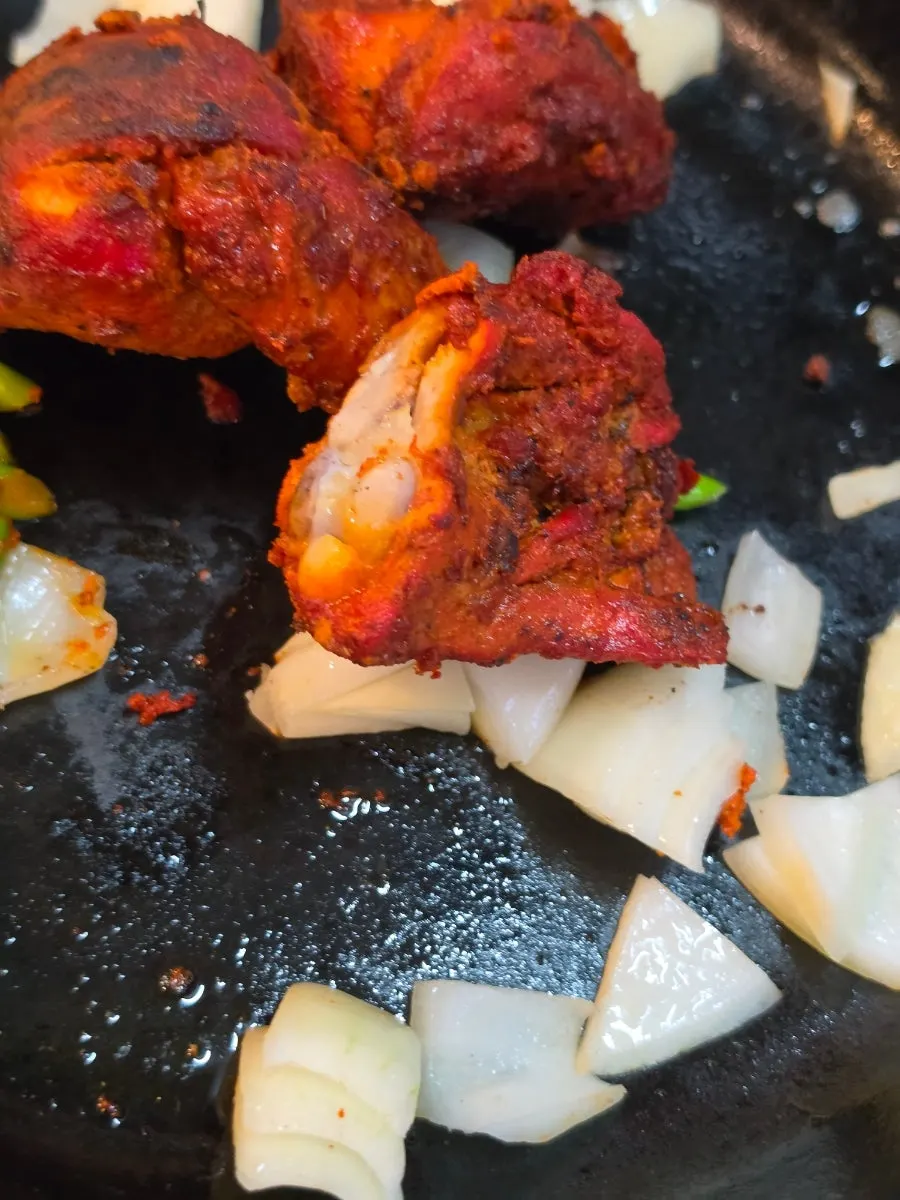 Tandoori chicken placed on onions and garlic scapes