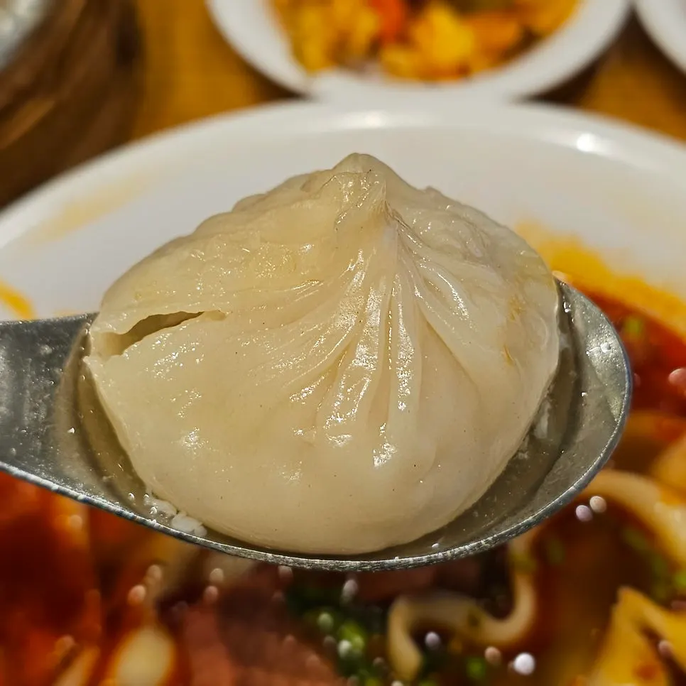 A xiaolongbao on a spoon with dim sum soy sauce