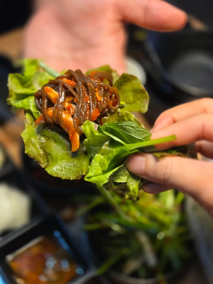 A large wrap loaded with meat and makguksu on a lettuce leaf