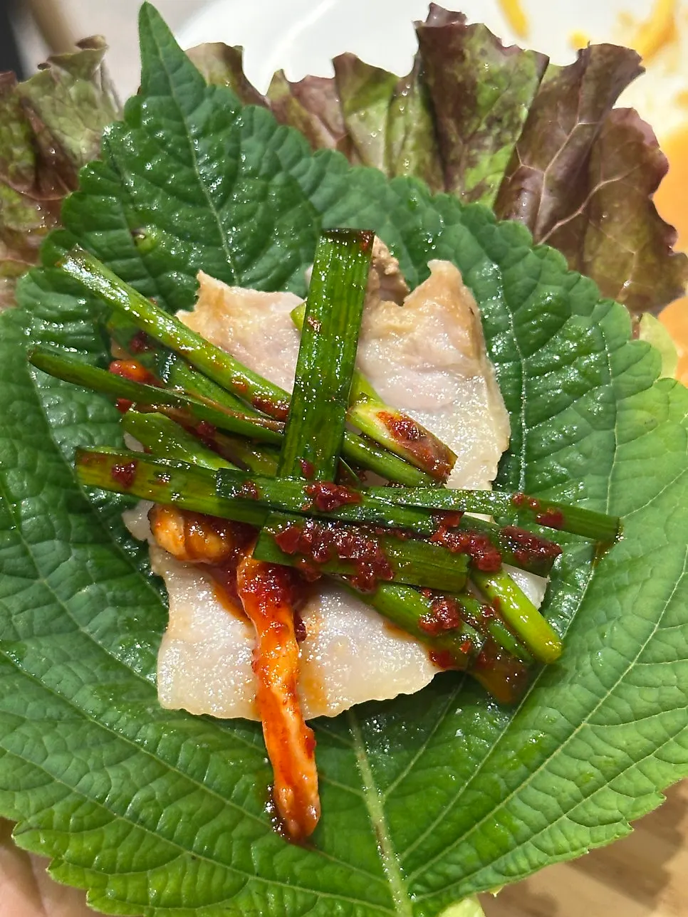 A wrapped bite of bossam topped with garlic and cheongyang chili