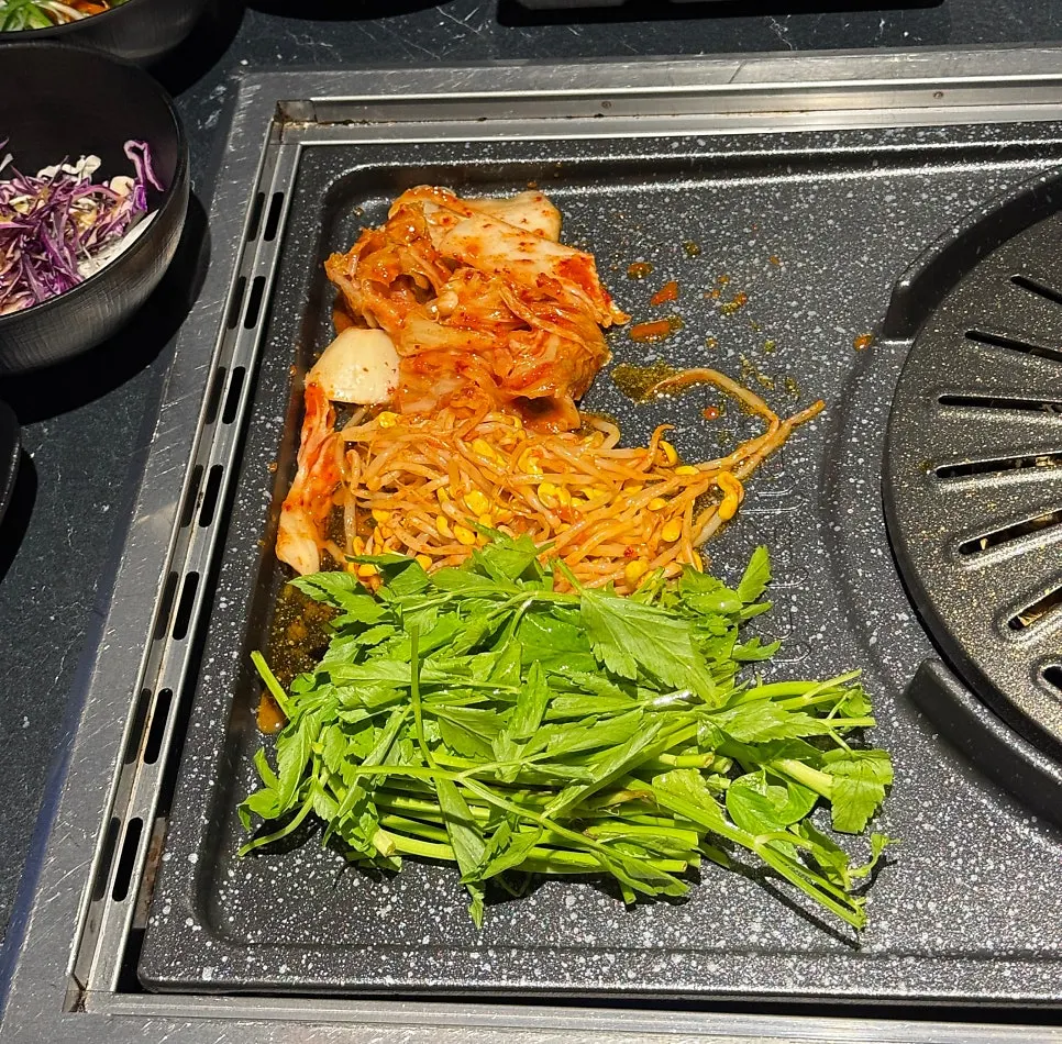 불판 한쪽에 올린 쑥과 콩나물무침, 김치