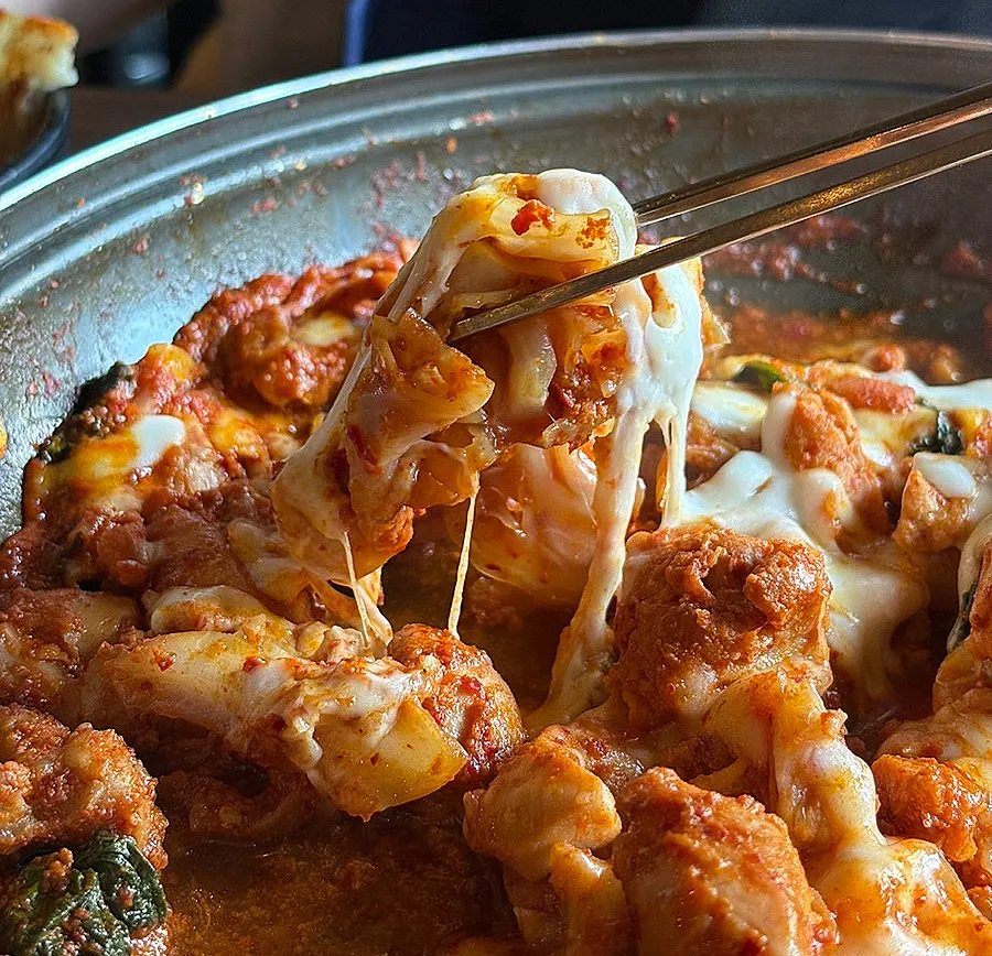 Close-up of dakgalbi with cheese draped over it on the grill
