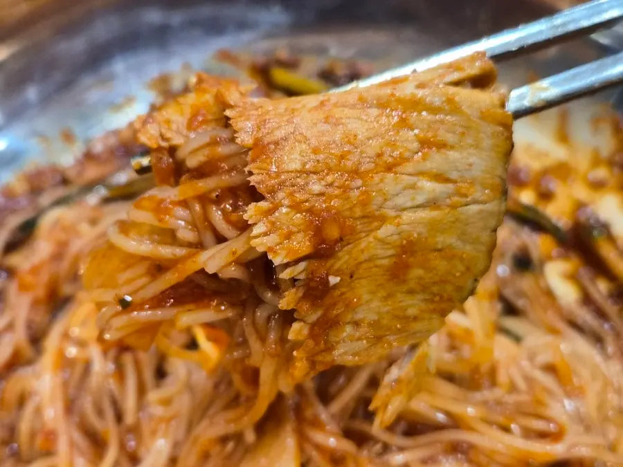 Chopsticks lifting a strand of bibim milmyeon noodles