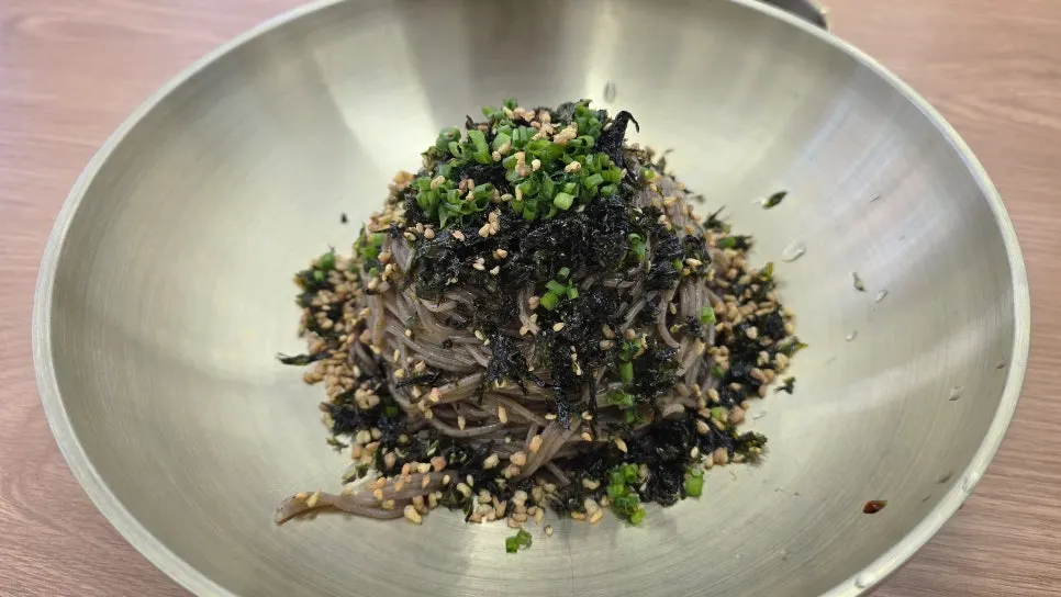 A bowl of perilla oil makguksu topped with sesame and seaweed