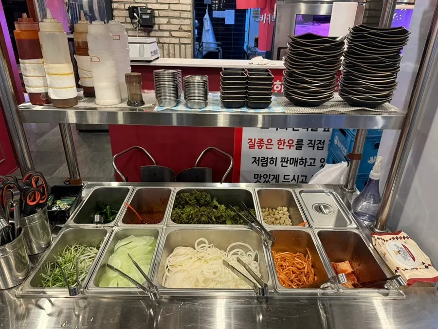 Self-serve bar with lettuce, vegetables, kimchi, and seasoned side dishes